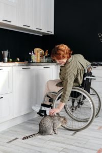 woman in a wheelchair petting a cat in a kitchen